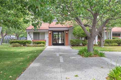 The image shows a building with a red roof and a tree in front of it.