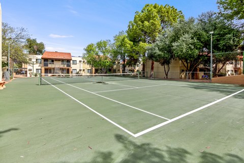 A tennis court surrounded by trees and buildings.
