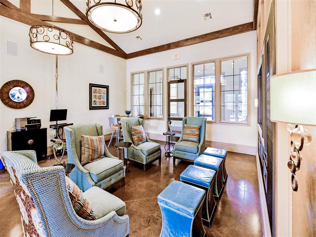 Interior of the community clubhouse, with a lounge area, blue chairs, and tall windows at Mission at La Villita Apartments, Texas