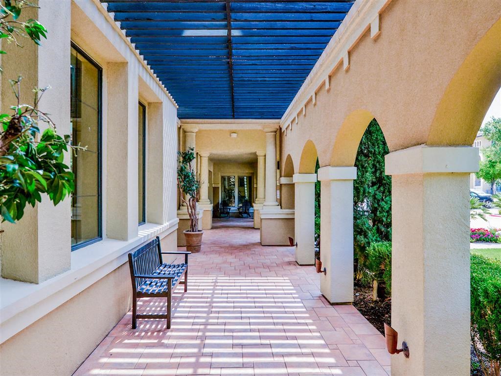 Exterior of apartment with paved walking paths, tan archways, and black bench at Mission at La Villita Apartments, Texas, 75039