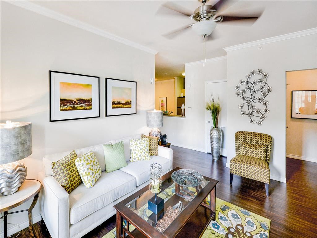 Living room view with plank flooring and white couch at Mission at La Villita Apartments, Irving, Texas