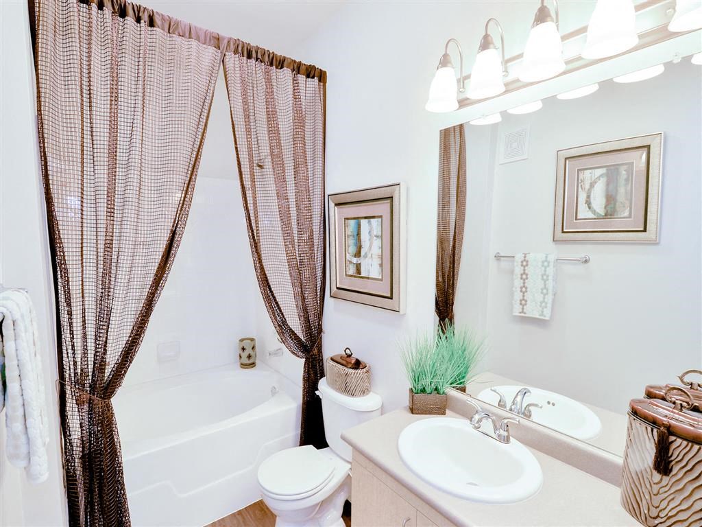 Spacious bathroom with tan counter top, white fixtures, large mirror, and brown shower curtain at Mission at La Villita Apartments, Texas, 75039