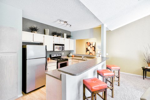 a kitchen with a bar and stools and a stainless steel refrigerator