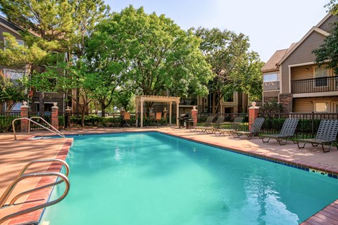 A swimming pool surrounded by trees and chairs.