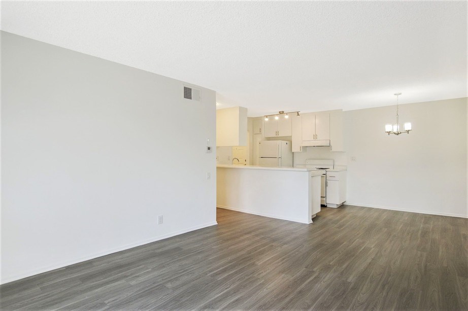 the living room and kitchen of an apartment with white walls and wood flooring