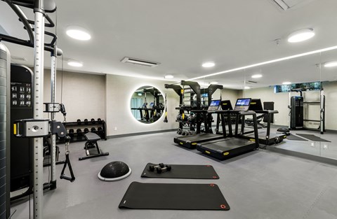 two treadmills and weights in a gym with a round mirror on the wall