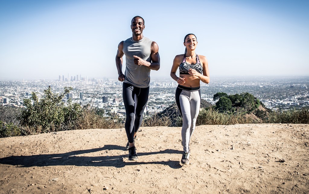 a man and a woman running on a dirt trail with a city in the background