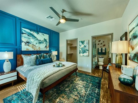 master bedroom with queen size bed and blue accent colored wall behind it. A door leads to the master bathroom and a second door shows the walk-in closet at Craft at Gilbert and Baseline Apartments, A