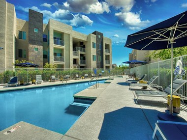 The Craft at Gilbert and Baseline Pool with buildings in the background and patio umbrella up front. Four lounge chairs line the pool.