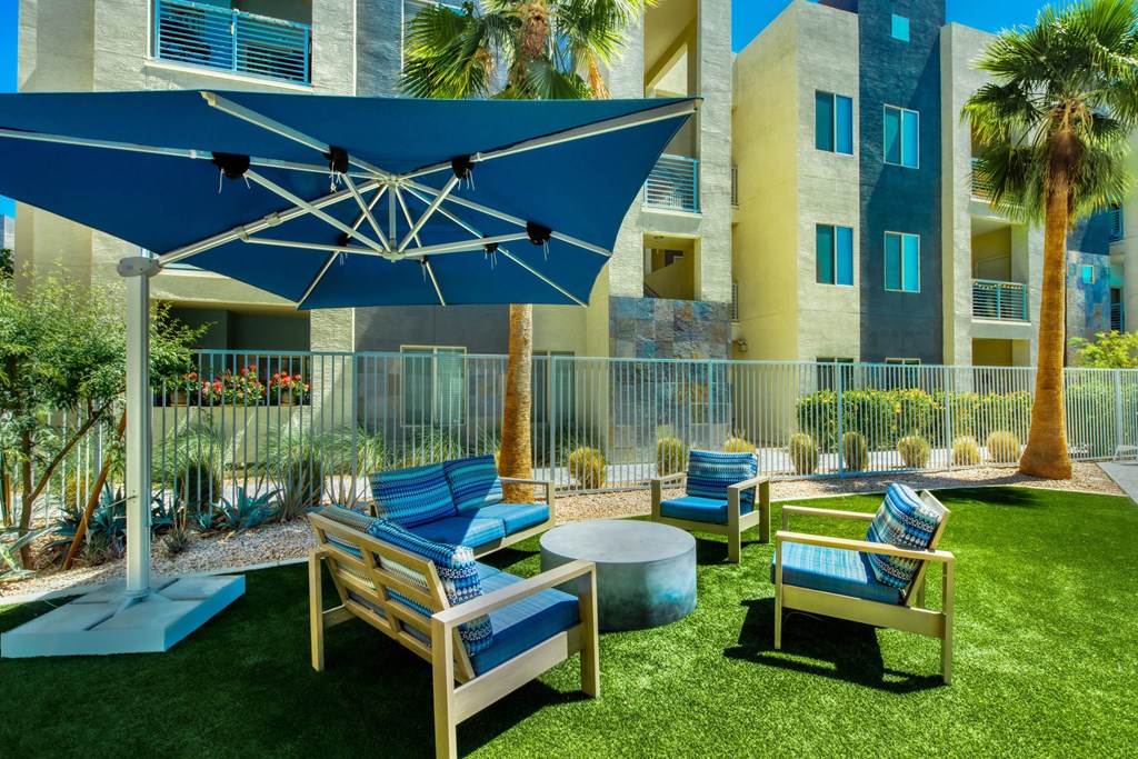 A blue umbrella shades a set of outdoor chairs.