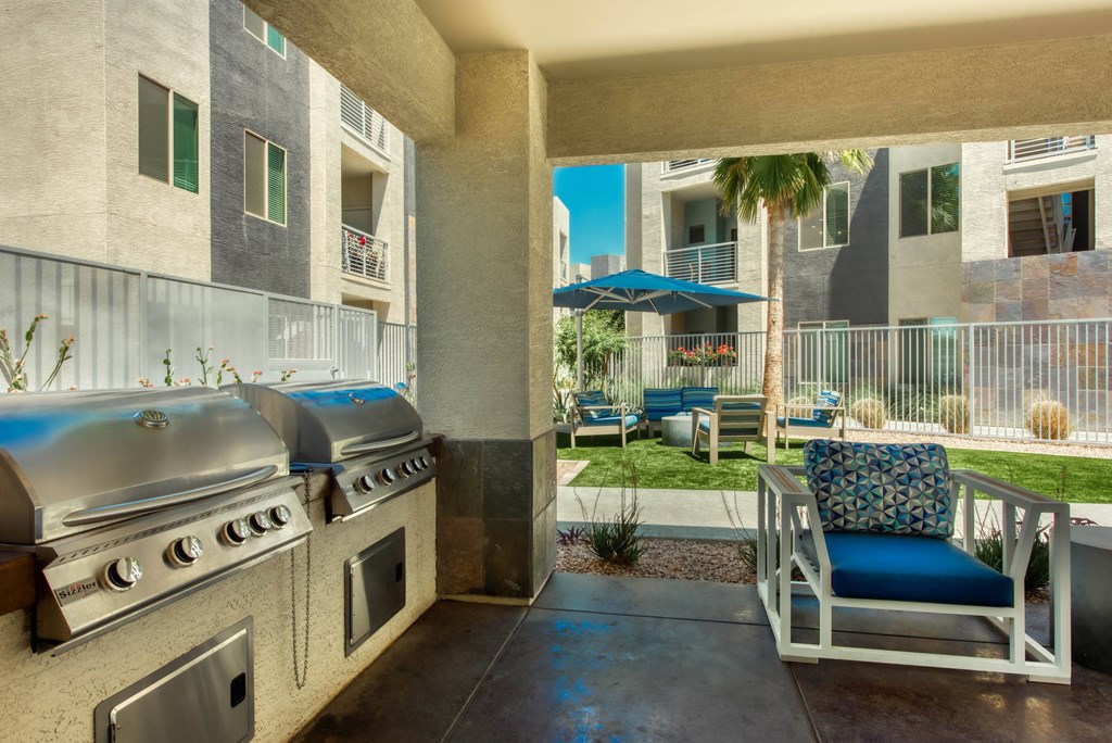A patio with a grill and a chair with a blue cushion.
