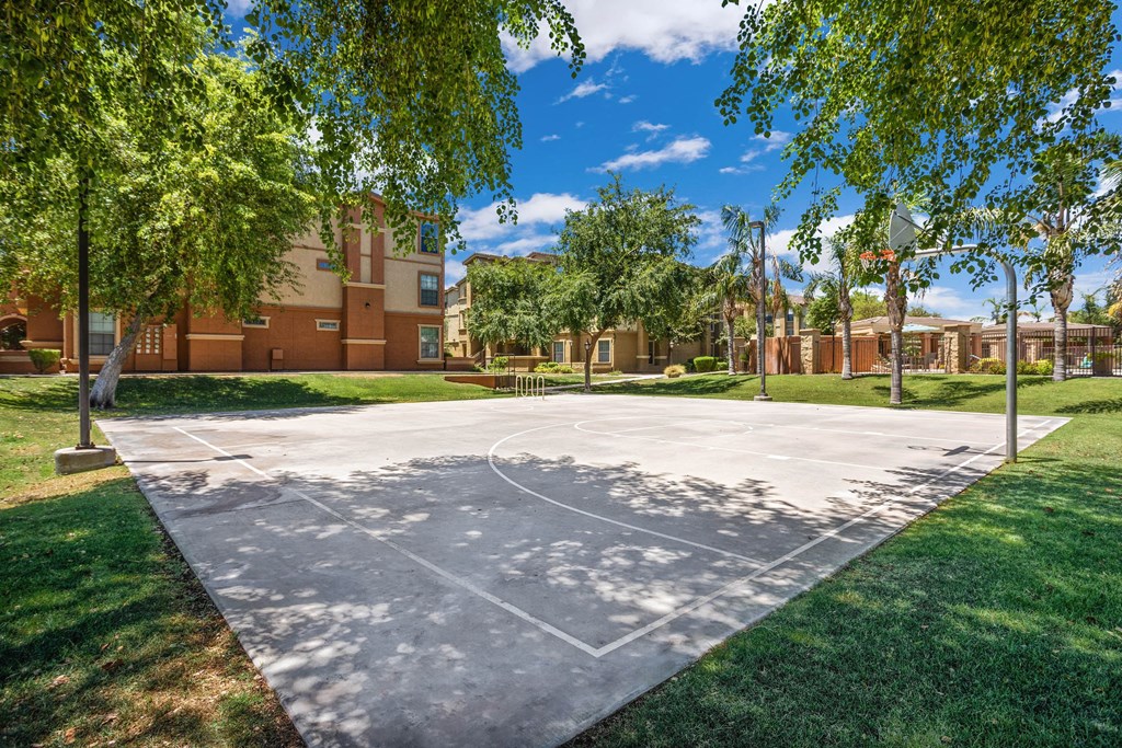 A basketball court is surrounded by trees and a building in the background.