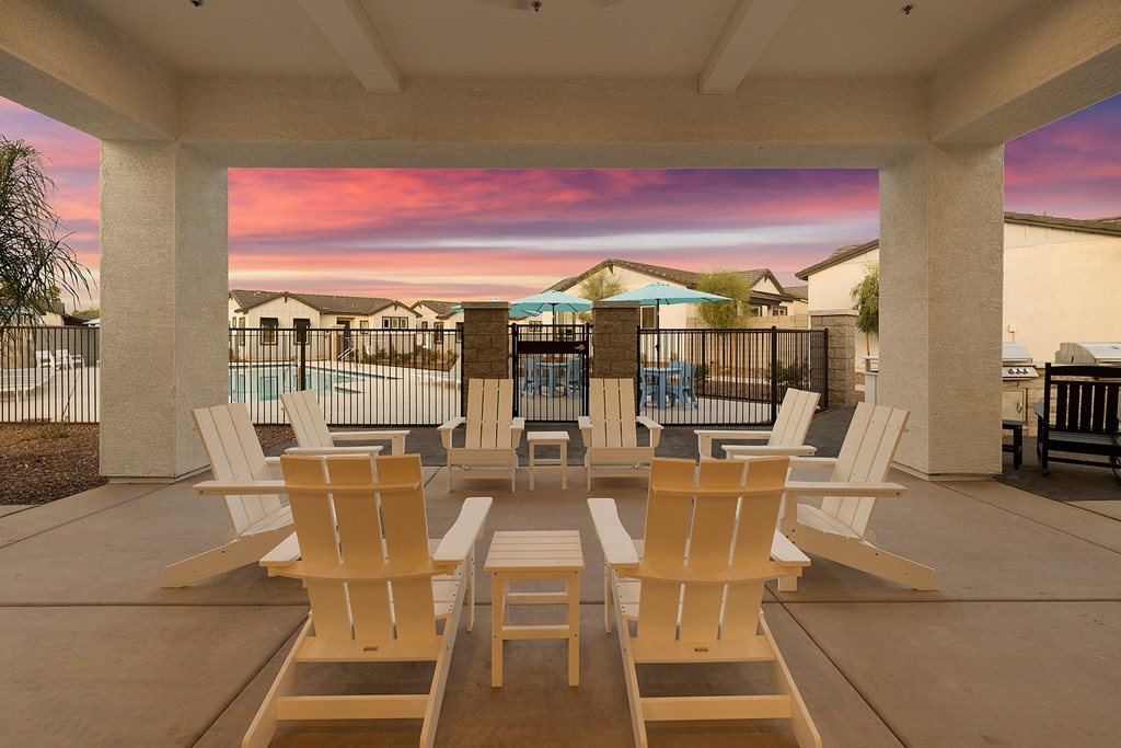 a patio with a table and chairs and a sunset over the pool