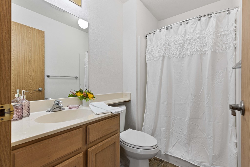 a bathroom with a white shower curtain and wooden cabinets