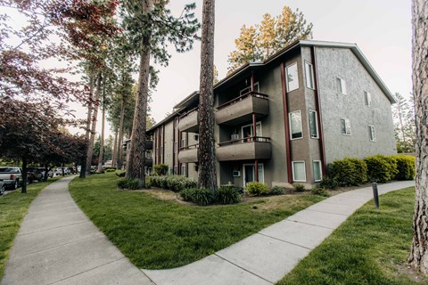 A concrete walkway leads to a two-story apartment building with a balcony on the second floor.
