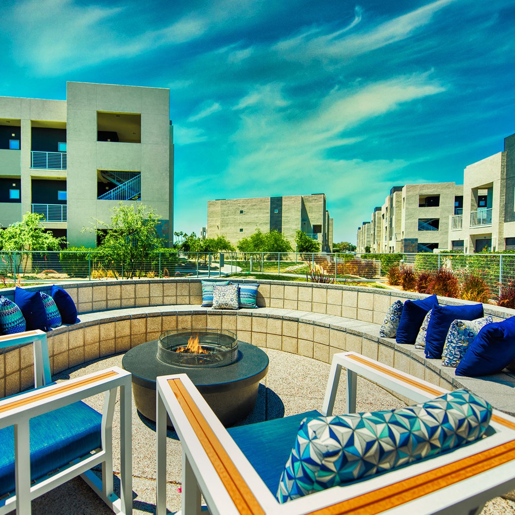 A patio with a fire pit and chairs with blue cushions.