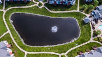 an aerial view of a lake in the middle of a green field and a house