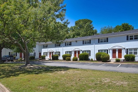 A white building with red doors and windows is surrounded by greenery.
