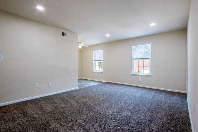 A spacious room with carpeted floor and two windows.