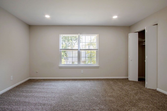 A room with a carpeted floor and a window with a view of trees outside.
