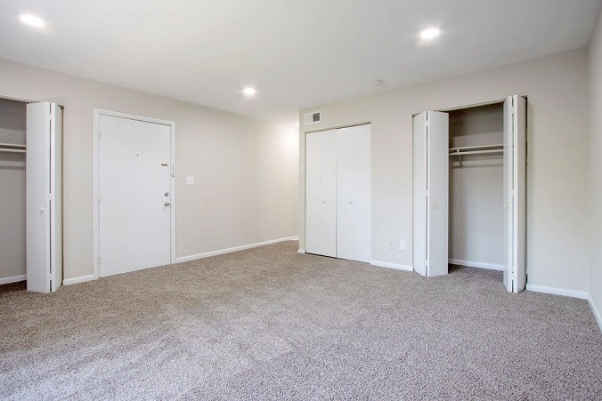 A room with white walls and carpeted floor with three white doors.