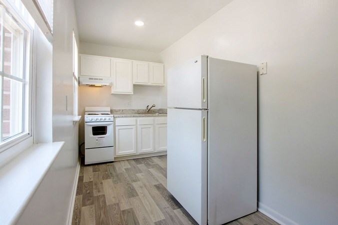 A white refrigerator stands in a kitchen with wooden floors and white cabinets.