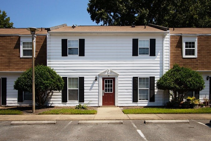A white house with a brown roof and a red door.