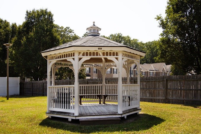 A gazebo with a black roof is surrounded by a wooden fence.
