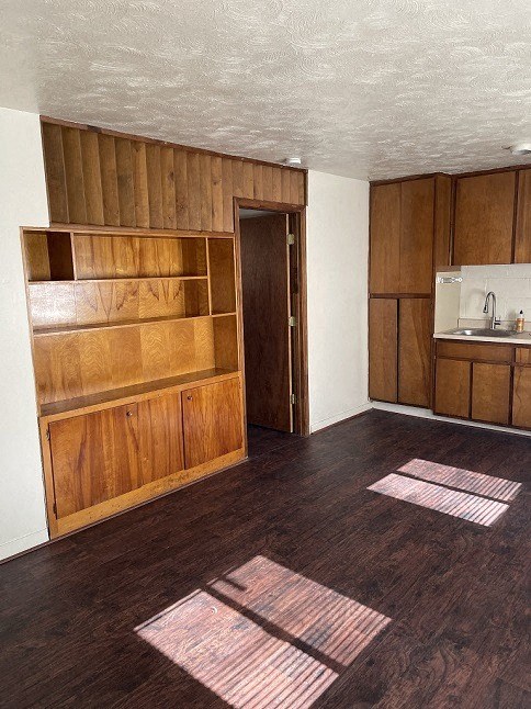 an empty living room with wooden floors and a kitchen