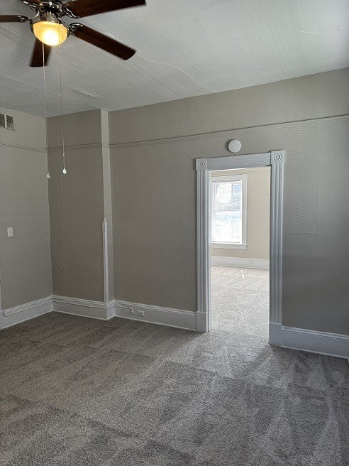 A room with a ceiling fan and carpeted floor.