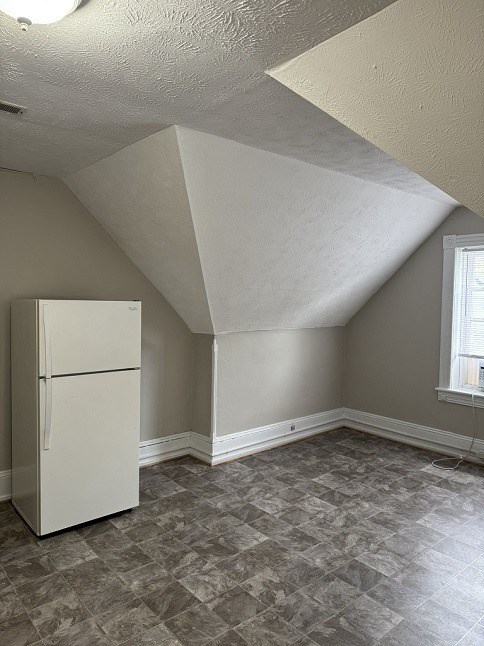 A room with a white fridge and a window.