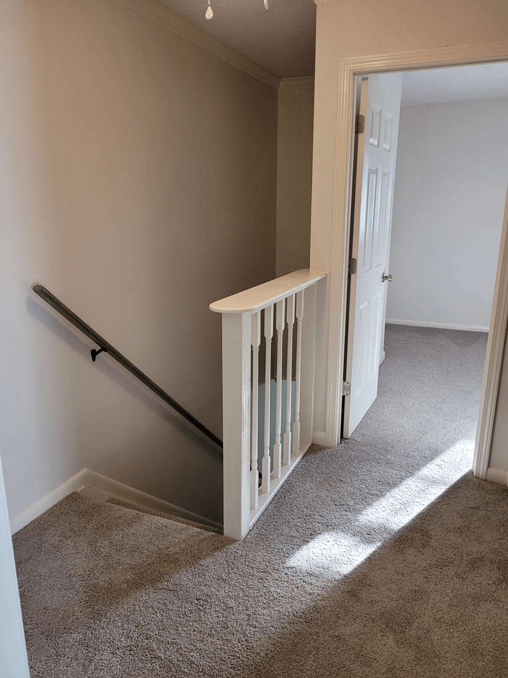 a stairway leading up to a hallway with a railing and a white carpet floor