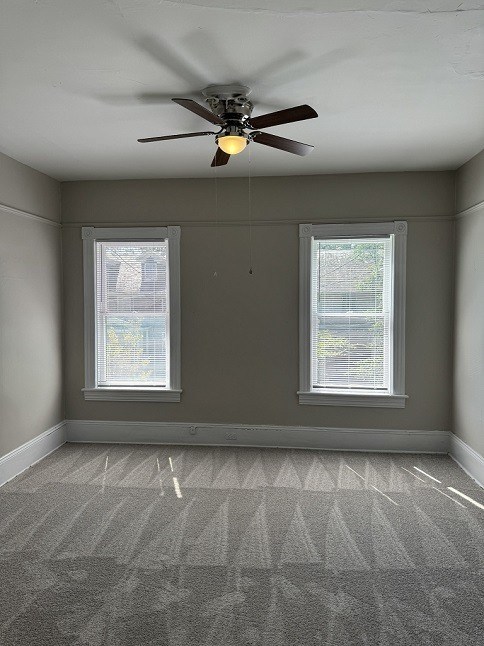 A room with a ceiling fan and two windows.