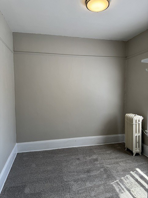 A room with a white radiator and carpeted floor.