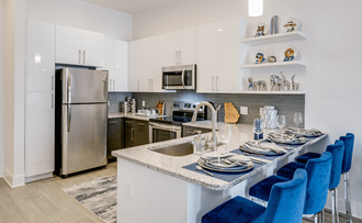 a kitchen with white cabinets and a large island with a granite countertop and blue chairs  at Link Apartments® Mixson, South Carolina - Photo Gallery 5