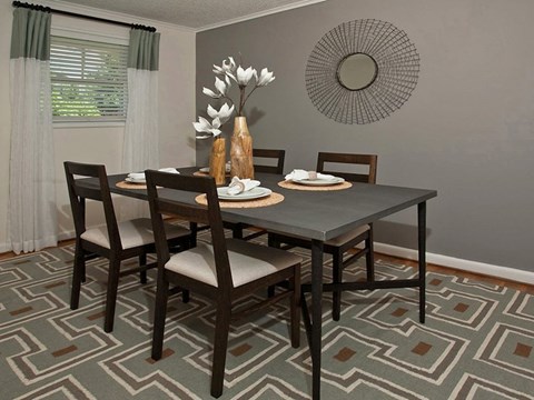 A dining room with a table set for two and a vase of white flowers.