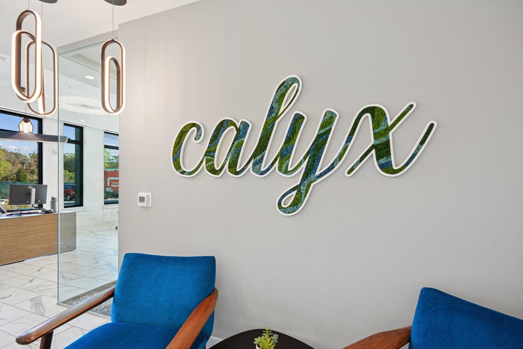 a large neon sign on the wall of a lobby with blue chairs at Link Apartments® Calyx, Chapel Hill