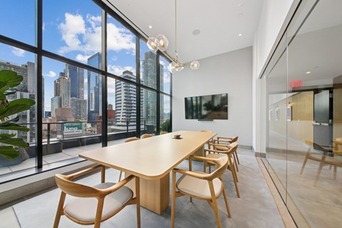 A conference room with a long table and chairs with a view of the city outside the window at Link Apartments® QPN, Long Island City, New York