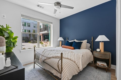 A bedroom with a bed, nightstand, and a plant.