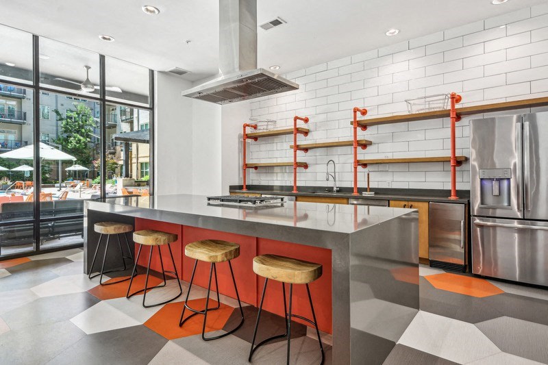 the kitchen has a large island with orange stools and stainless steel appliances at Link Apartments Innovation Quarter, Winston Salem, 27101