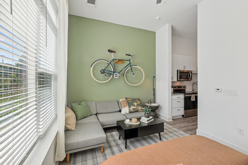A living room with a grey couch and a bicycle on the wall at Link Apartments® CYKEL Apartments, North Carolina