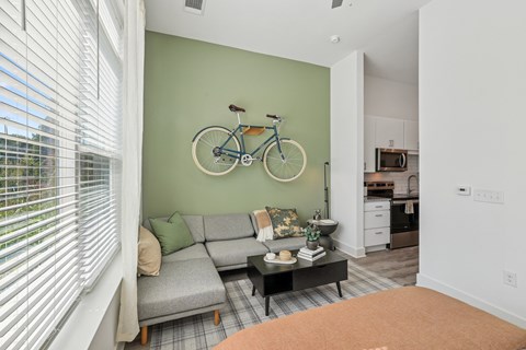A living room with a grey couch and a bicycle on the wall.