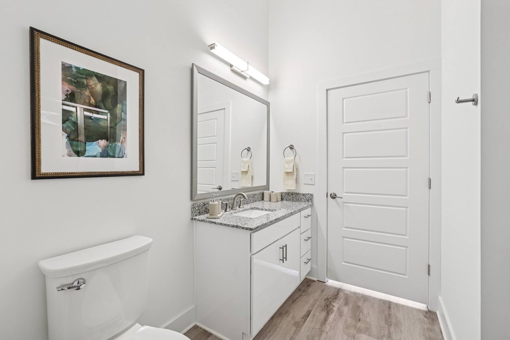 A white bathroom with a toilet, sink, and mirror at Link Apartments® CYKEL Apartments, Charlotte, NC