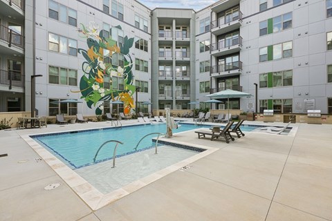 A pool surrounded by apartment buildings with a mural of a plant on the side.