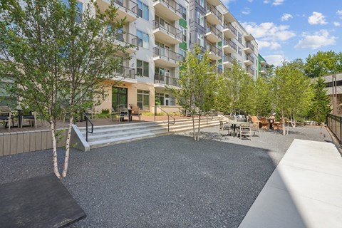 A playground area with a slide, swings, and a tree in front of a multi-story apartment building.