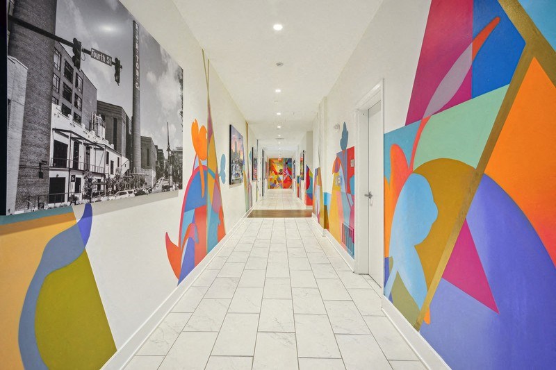 a hallway with colorful paintings on the walls and a white tile floor at Link Apartments® 4th Street, North Carolina, 27101