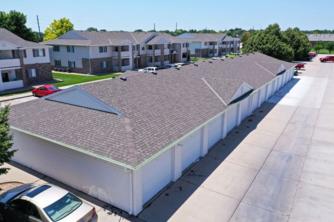 A long white building with a grey roof is surrounded by cars and other buildings.