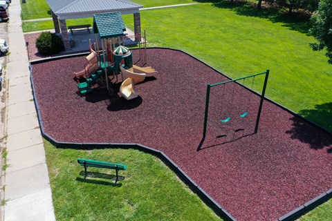 A playground with a red rubber surface and a green slide.
