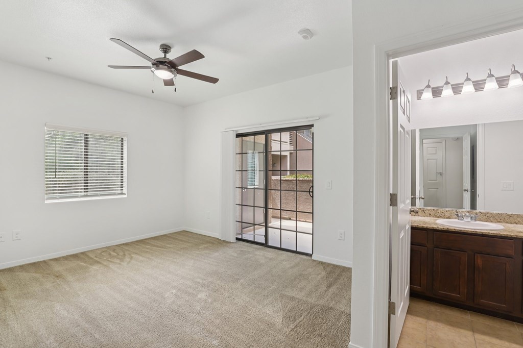 A spacious room with a ceiling fan and a sliding glass door leading to a backyard.