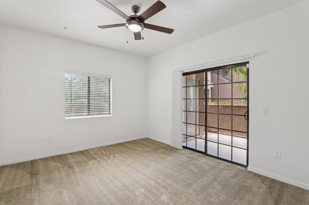 A room with a ceiling fan and a sliding glass door leading to a balcony.